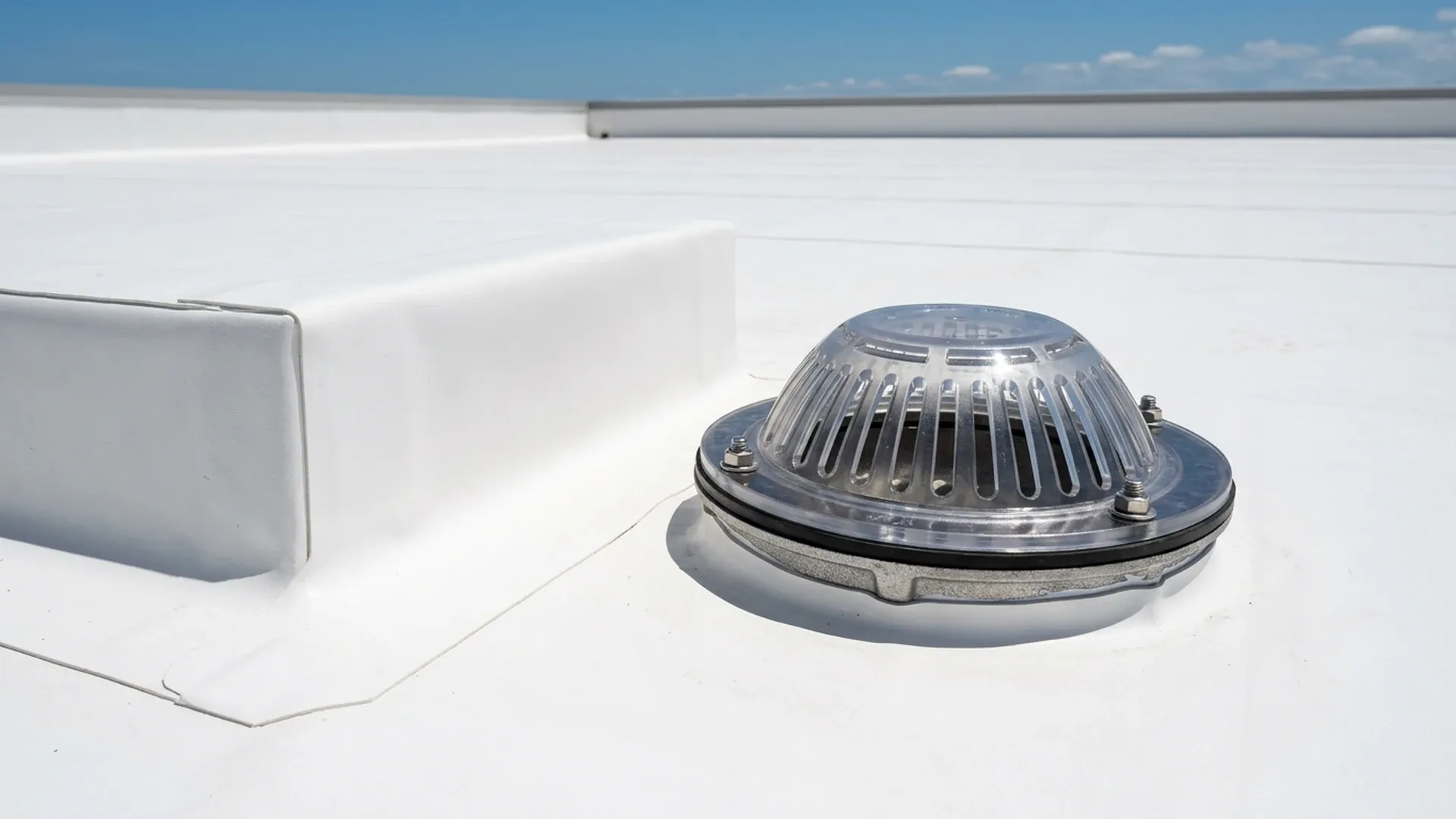 Roof drain and curb detail on a white commercial flat roof with the membrane flashed up the curb and no standing water
