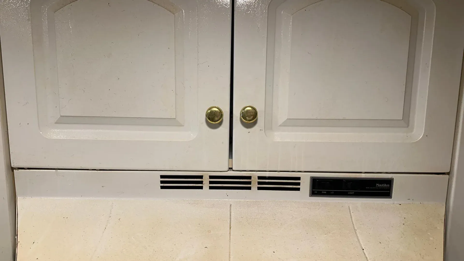 Grimy ledge and vent below white kitchen cabinets that need a deep cleaning service in Tampa Bay