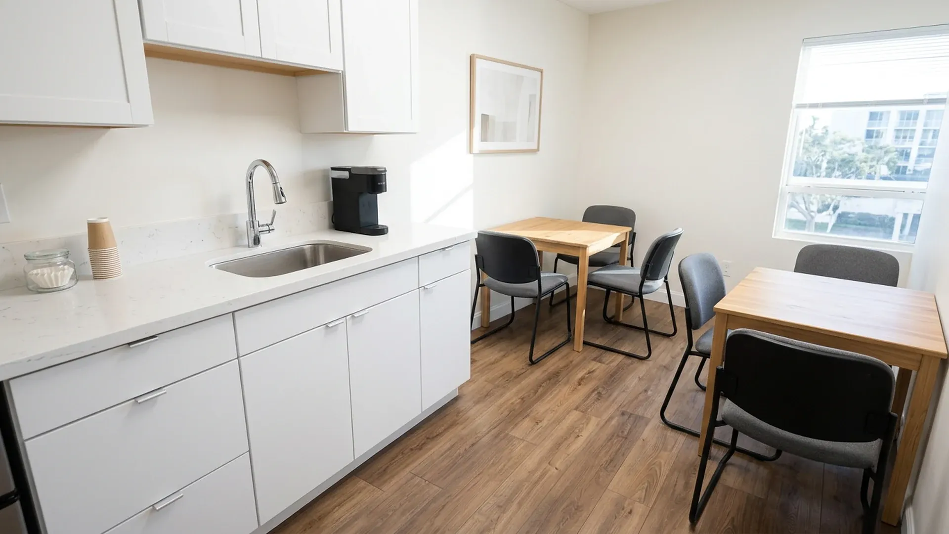 Clean office breakroom with a quartz countertop, stainless steel sink, coffee maker and wiped tables.