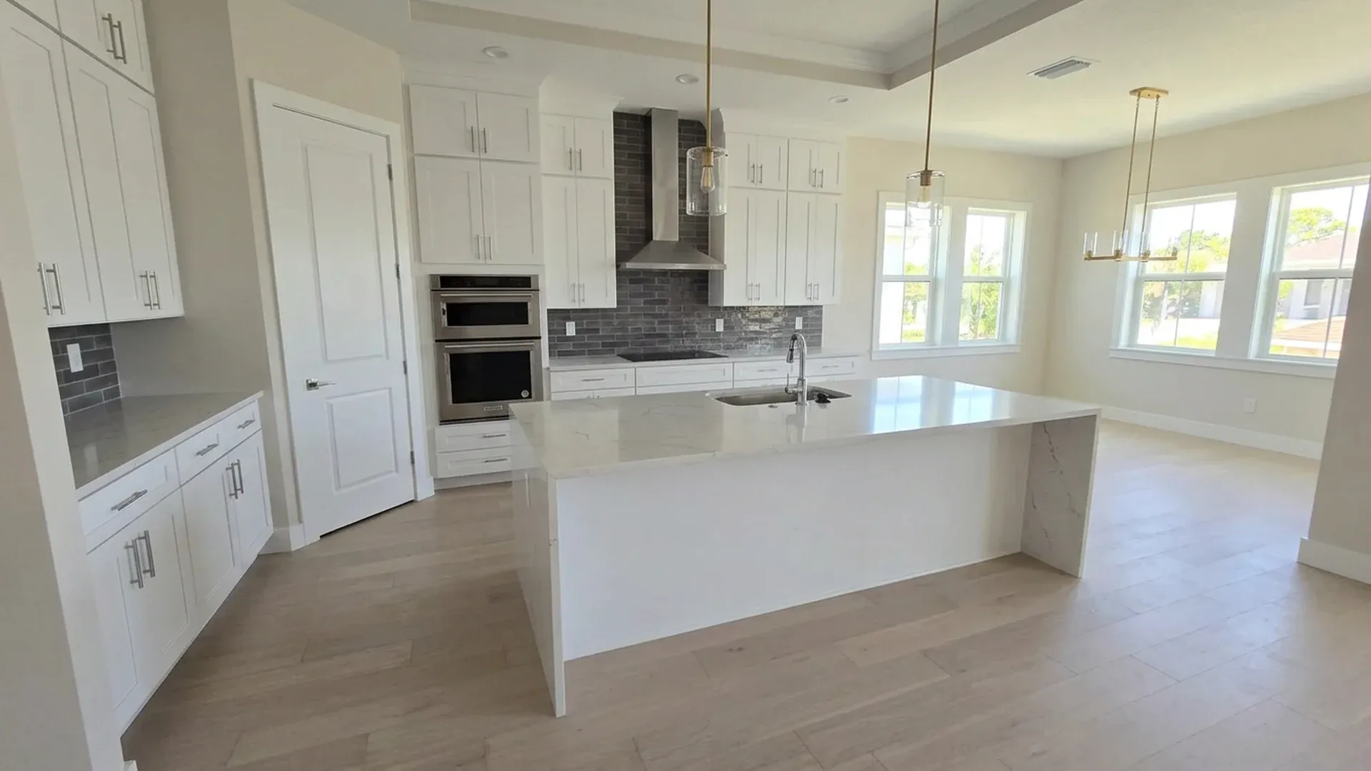 Clean remodeled kitchen with white shaker cabinets, quartz waterfall island and pendant lights.